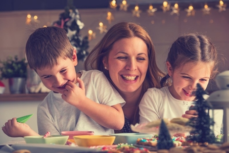 A smiling mother and two children happily decorate holiday treats in a festive setting