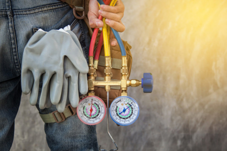 A technician with gloves uses red and blue gauges to check an outdoor AC unit.