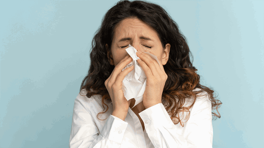 A woman with curly dark hair blows her nose into a tissue