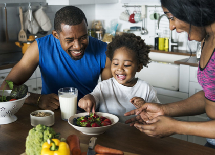 A happy family in their kitchen smiles while preparing healthy food.