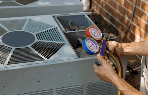 A technician's hands connect red and blue gauges to an outdoor air conditioning unit,