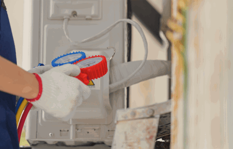 A technician in white gloves uses a manifold gauge set to service an outdoor air conditioning unit.
