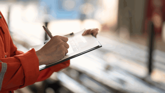 A technician in an orange uniform writes on a clipboard