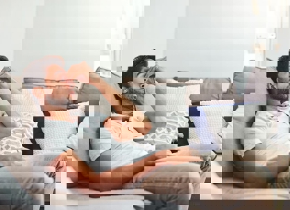 A man lies on a sofa, holding his forehead in discomfort