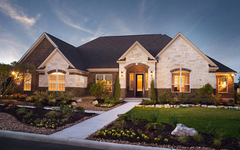 A beautiful single-story home is illuminated at dusk, showcasing its brick and stone exterior.