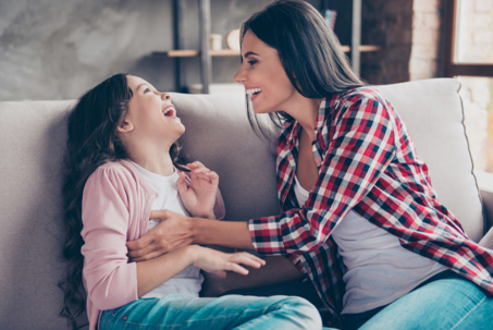 A mother and daughter share a joyful, comfortable moment on a sofa.