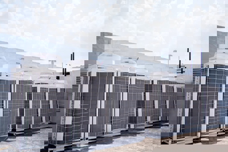 Six commercial HVAC units are lined up on a rooftop under a sunny sky.