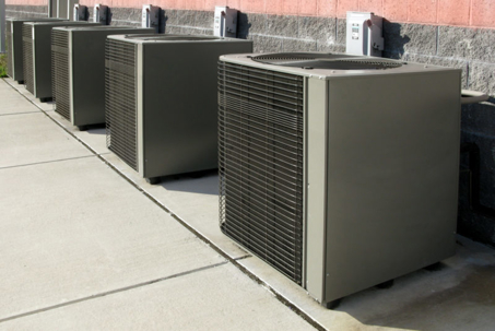 Five commercial HVAC outdoor condenser units are neatly lined up along a brick building wall on a concrete pad.