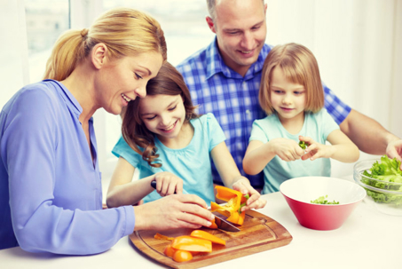 A happy family, two parents and two children, smiles as they prepare a healthy meal in their home kitchen.