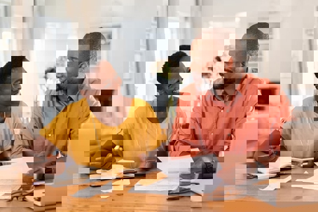A smiling couple sits at a wooden table with papers and laptop.