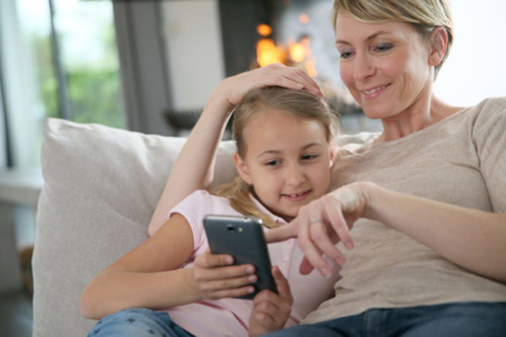 A mother and daughter comfortably share a smartphone on a couch.